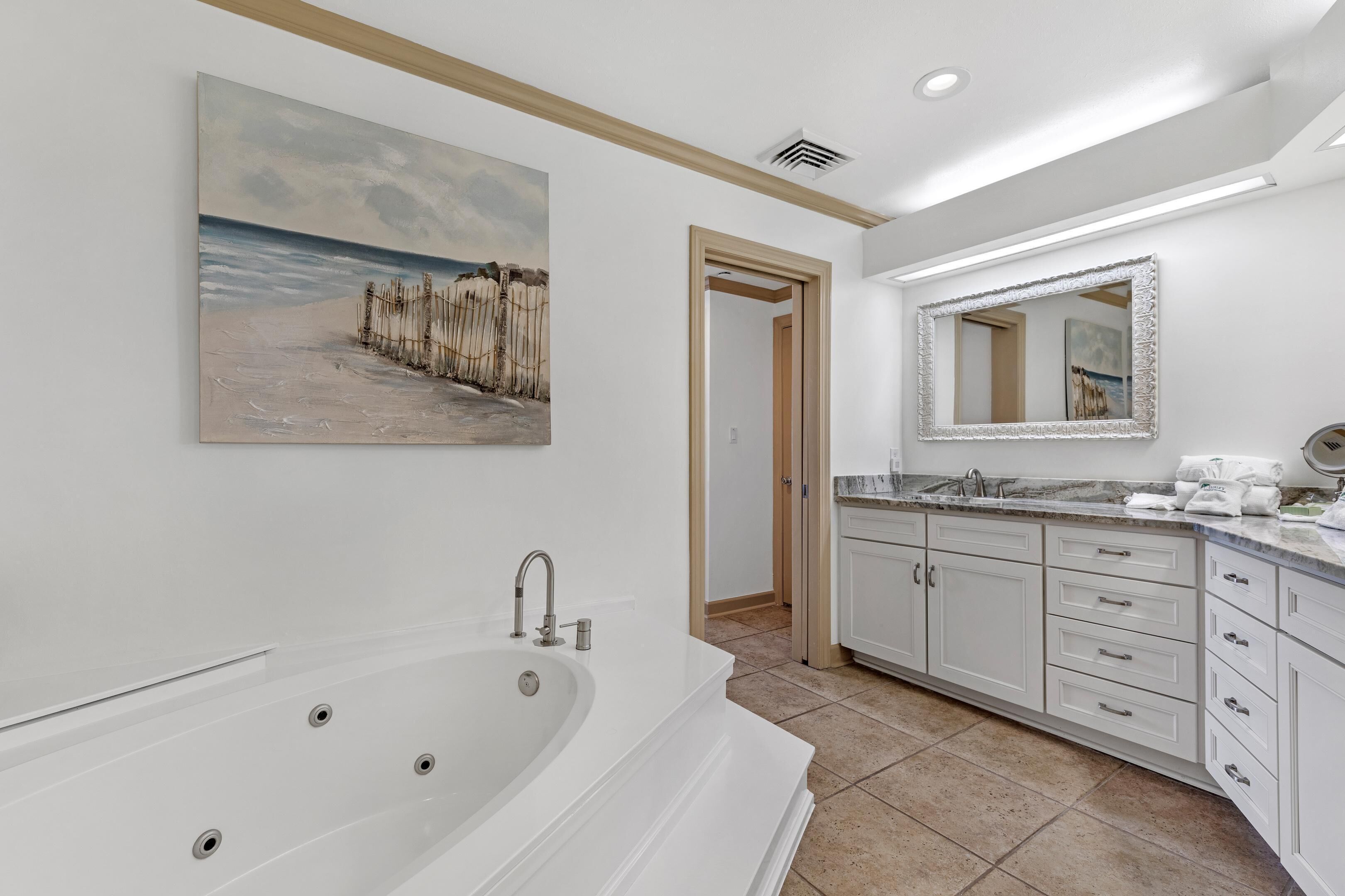 A modern bathroom with a large bathtub, a sink with a mirror, and a painting of a beach scene.