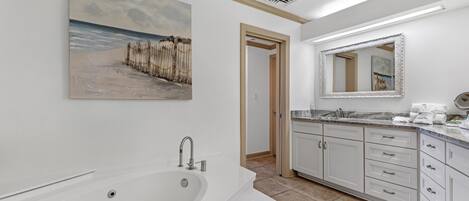 A modern bathroom with a large bathtub, a sink with a mirror, and a painting of a beach scene.