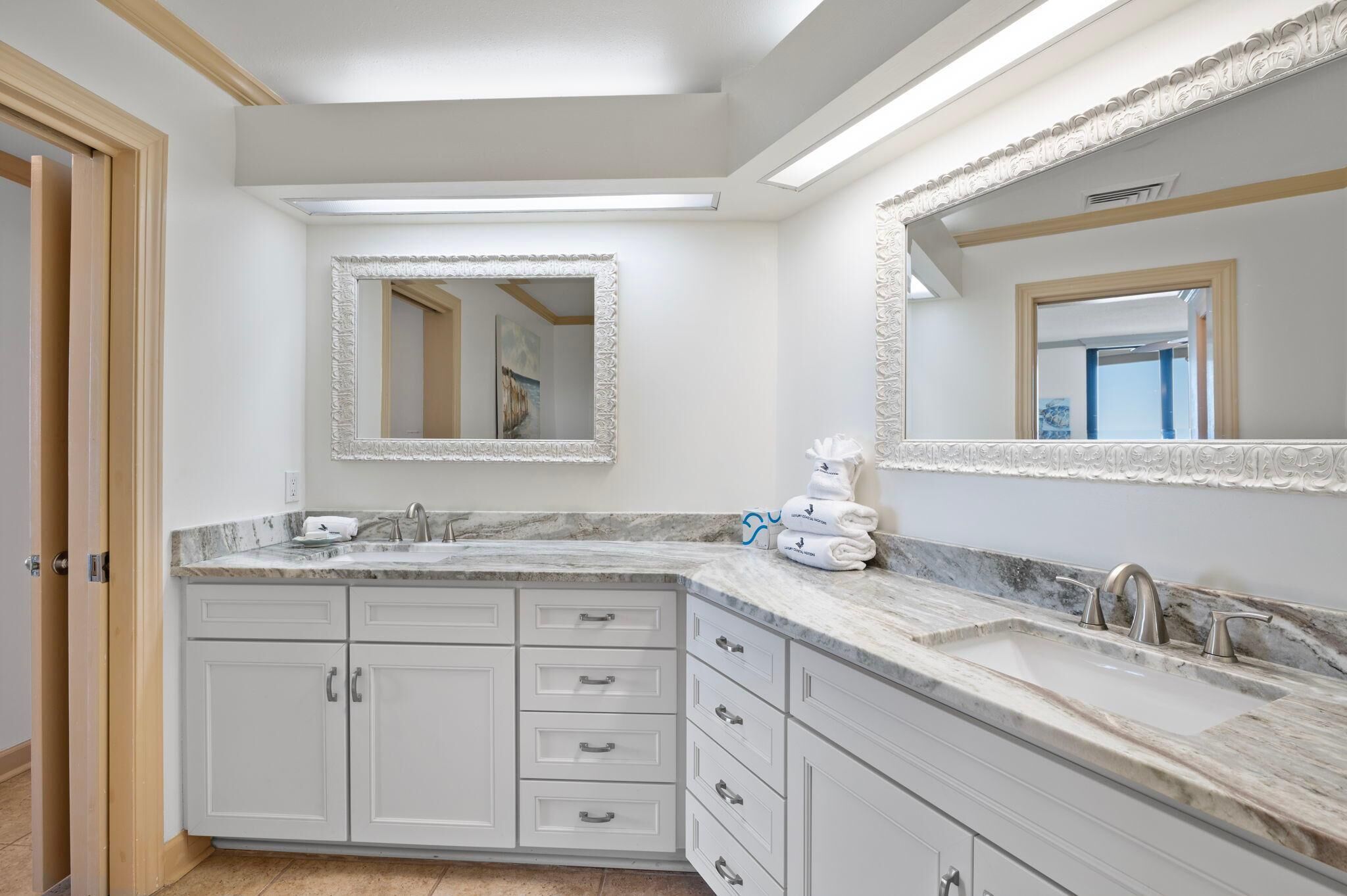 A modern bathroom with a large vanity, two sinks, and a mirror with an ornate frame.