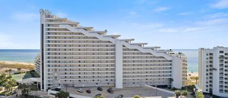 A multi-story hotel with a modern design, located near a beach with a clear view of the ocean.