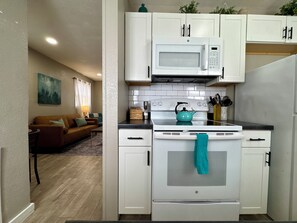 Une cuisine compacte avec des meubles blancs, un four à micro-ondes, une cuisinière et une bouilloire.