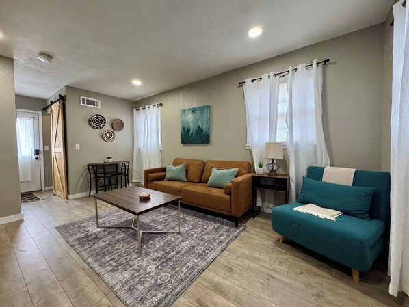 A living room with a brown sofa, a teal sofa, a wooden coffee table, and a patterned rug.