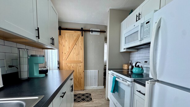 A compact kitchen with white cabinets, a black countertop, a teal kettle, and a white refrigerator. - Near Wichita Airport! Pet Friendly W/ Fenced Patio (Wichita)