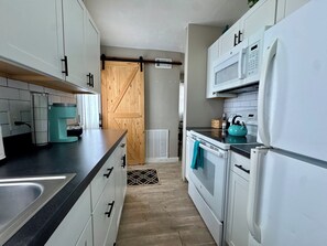 A compact kitchen with white cabinets, a black countertop, a teal kettle, and a white refrigerator.