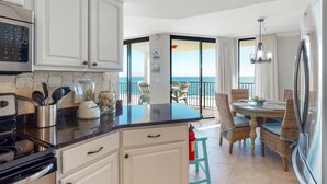 A kitchen with white cabinets, a black countertop, and a view of the ocean through a sliding glass door. - Phoenix VII 1002 (Orange Beach)