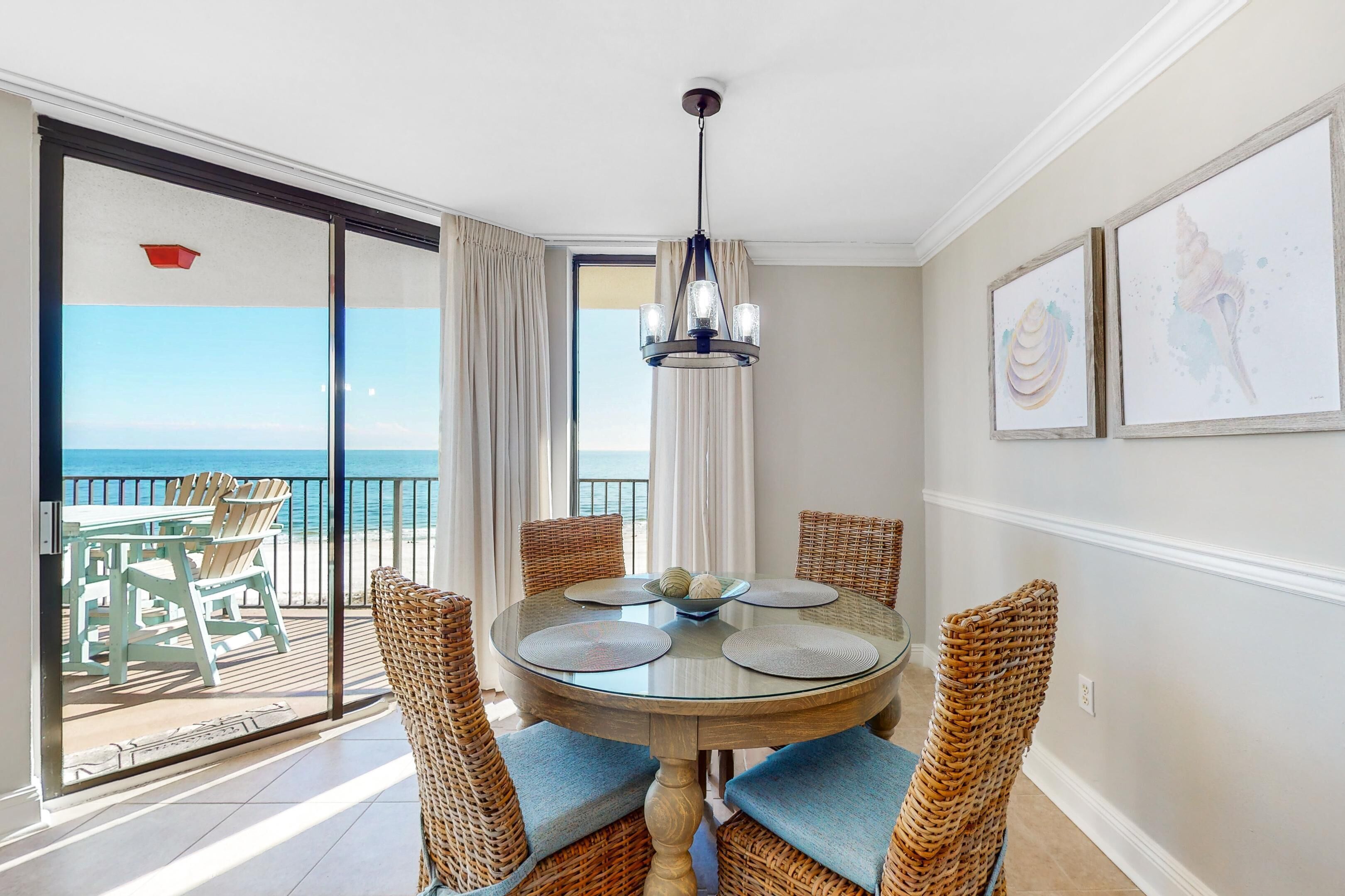 A dining area with a round glass table, wicker chairs, and a view of the ocean through a sliding glass door.