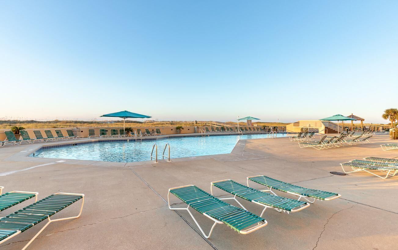 A pool area with lounge chairs and umbrellas, a clear sky, and a distant view of a building.