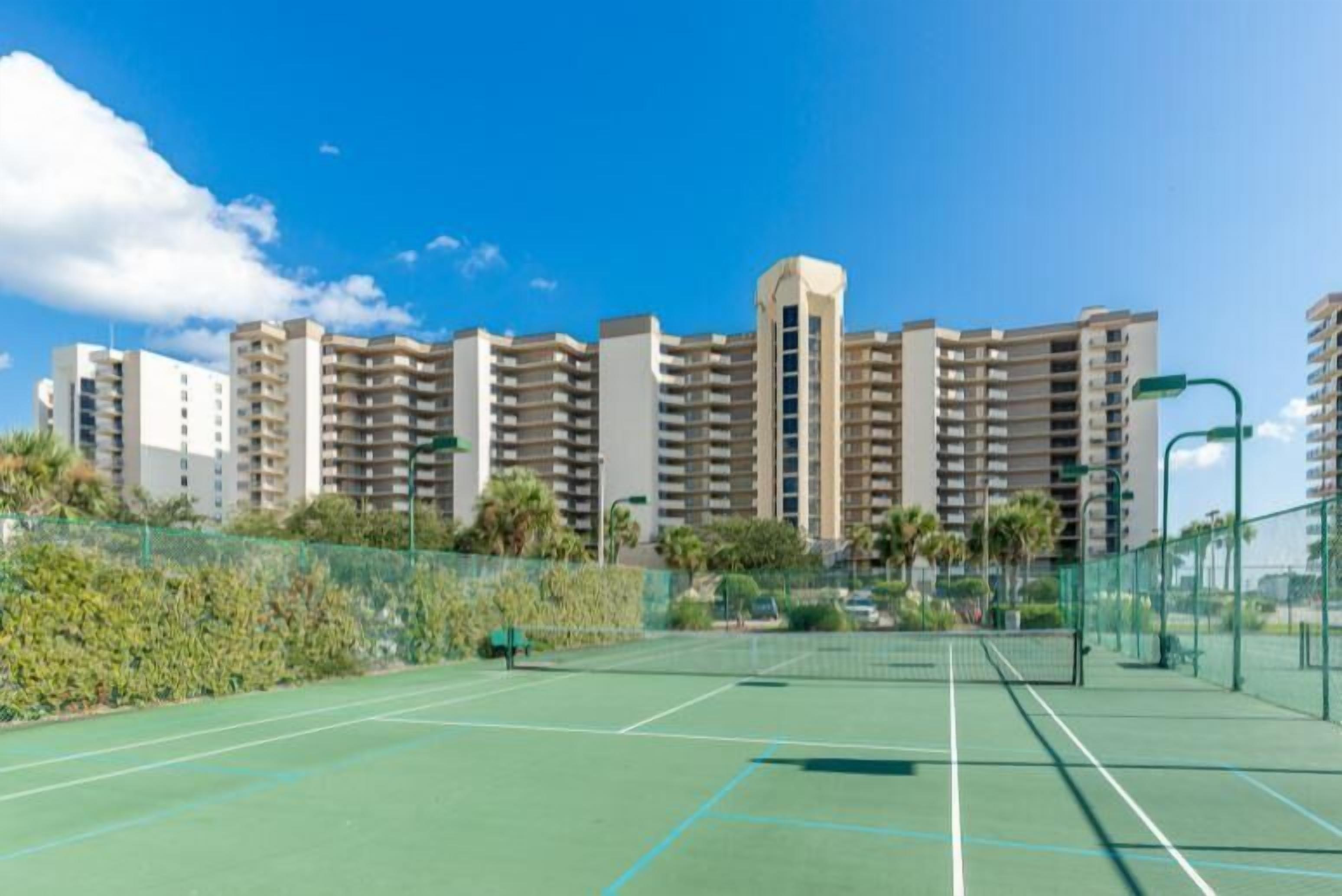 Un court de tennis avec un filet, entouré d’une clôture et de palmiers.