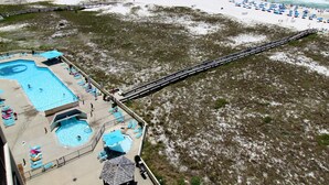 An aerial view of a beach resort with a swimming pool, beach umbrellas, and a boardwalk. - Phoenix VII 1002 (Orange Beach)