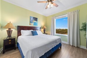 Relax in this serene bedroom with a large bed, nightstand, and ceiling fan, offering a peaceful view of the outdoors.