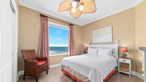 Une chambre à coucher avec un lit, une chaise, une table de chevet, une lampe et une vue sur l’océan.