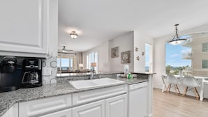 A modern kitchen with white cabinets, granite countertops, and a built-in coffee maker. - Beach Colony West 4D (Pensacola)