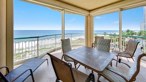 A balcony with a table and chairs, overlooking a beach and ocean. - Beach Colony West 4D (Pensacola)