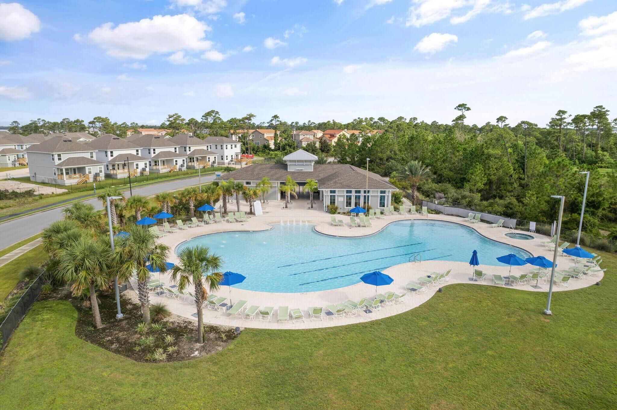 A swimming pool with lounge chairs and umbrellas, surrounded by a landscaped area with palm trees.