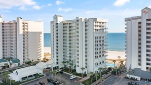 A beachfront hotel with multiple high-rise buildings, a parking area, and a clear view of the ocean. - Pelican Pointe 202 (Orange Beach)