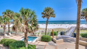 A pool area with palm trees, a beach view, and a wooden deck. - Pelican Pointe 202 (Orange Beach)