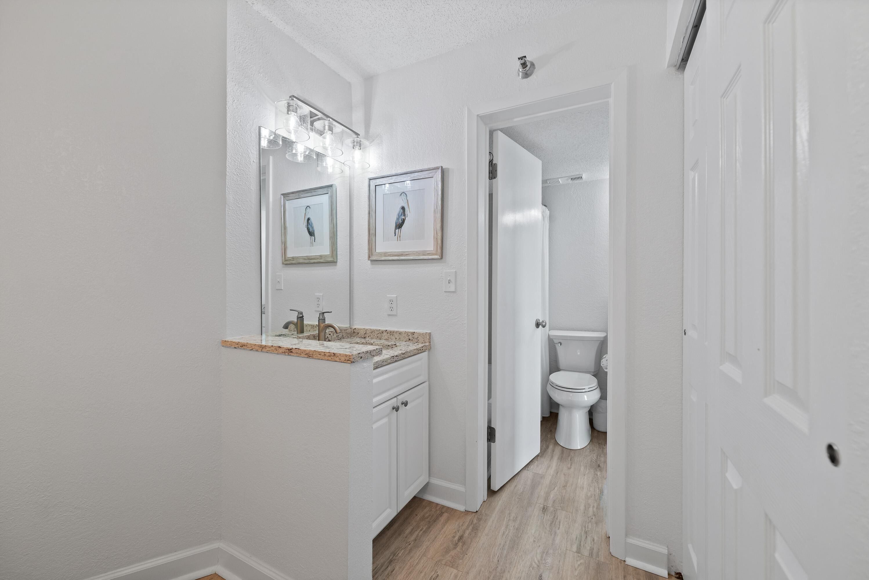 Ein Badezimmer mit weißem Waschtisch, einem Waschbecken und einer Toilette. Über dem Waschtisch hängen gerahmte Bilder an der Wand.