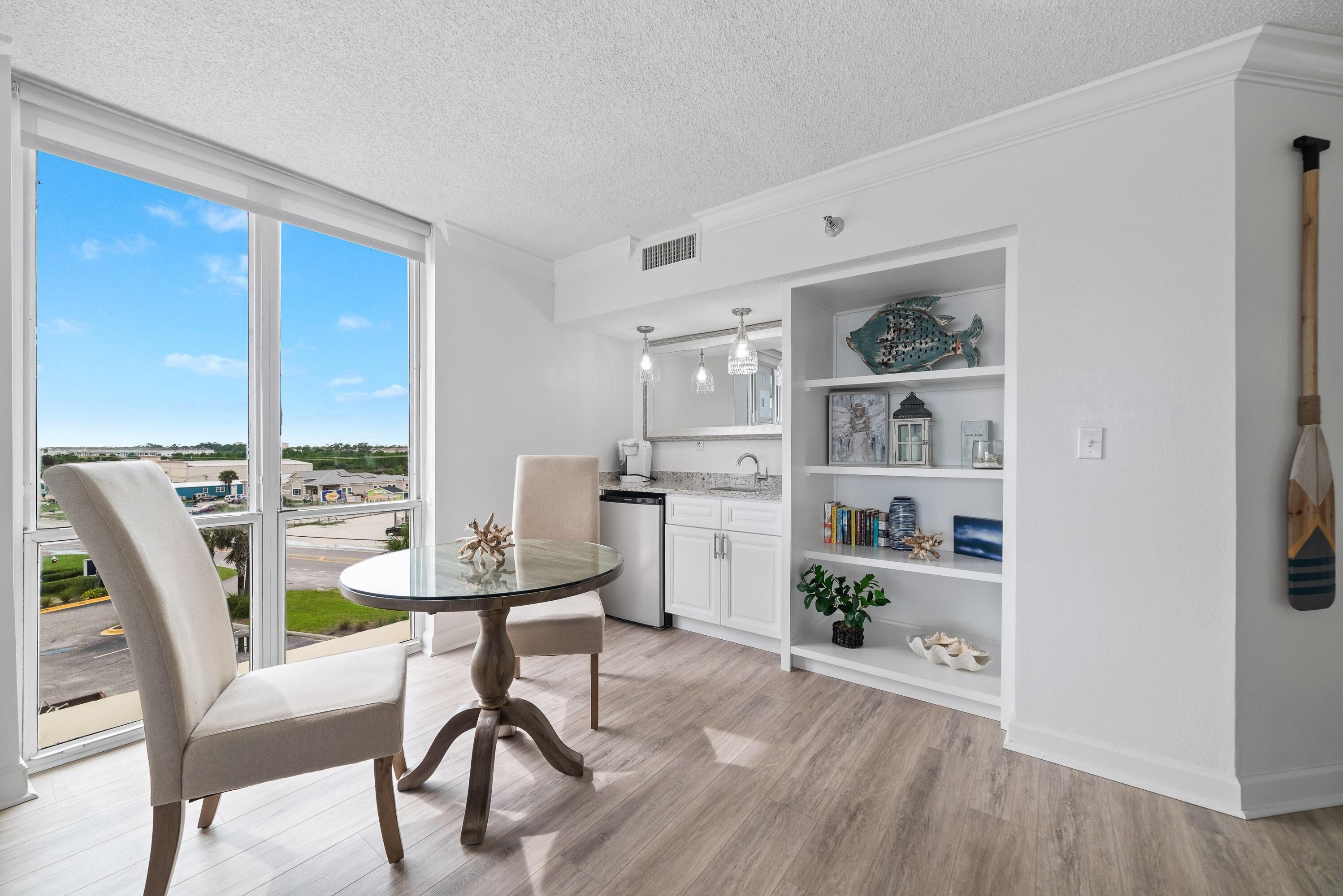 Una cocina moderna con armarios blancos, un comedor con mesa de vidrio y vista al exterior.