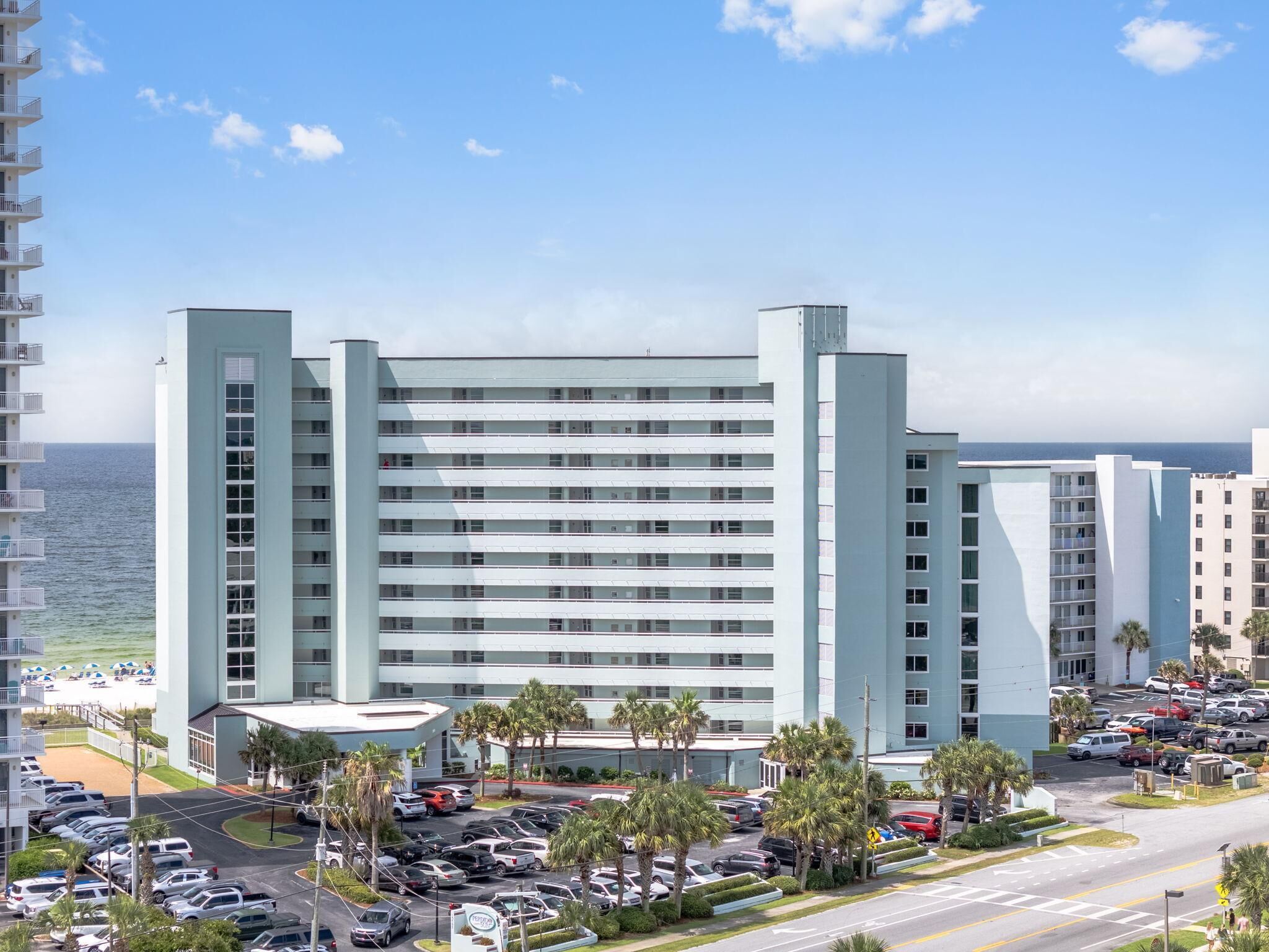 A multi-story hotel with a parking lot and a view of the ocean.
