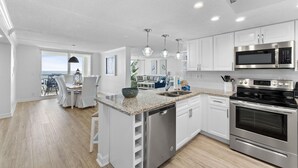 A modern kitchen with white cabinets, stainless steel appliances, and a granite countertop. - Perdido Sun 416 (Pensacola)