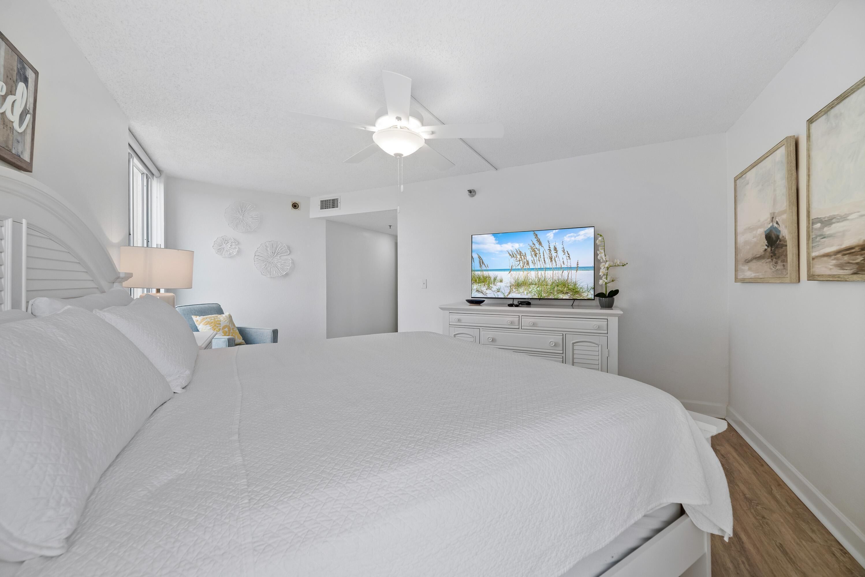 A bedroom with a large bed, a ceiling fan, a TV, and a window.
