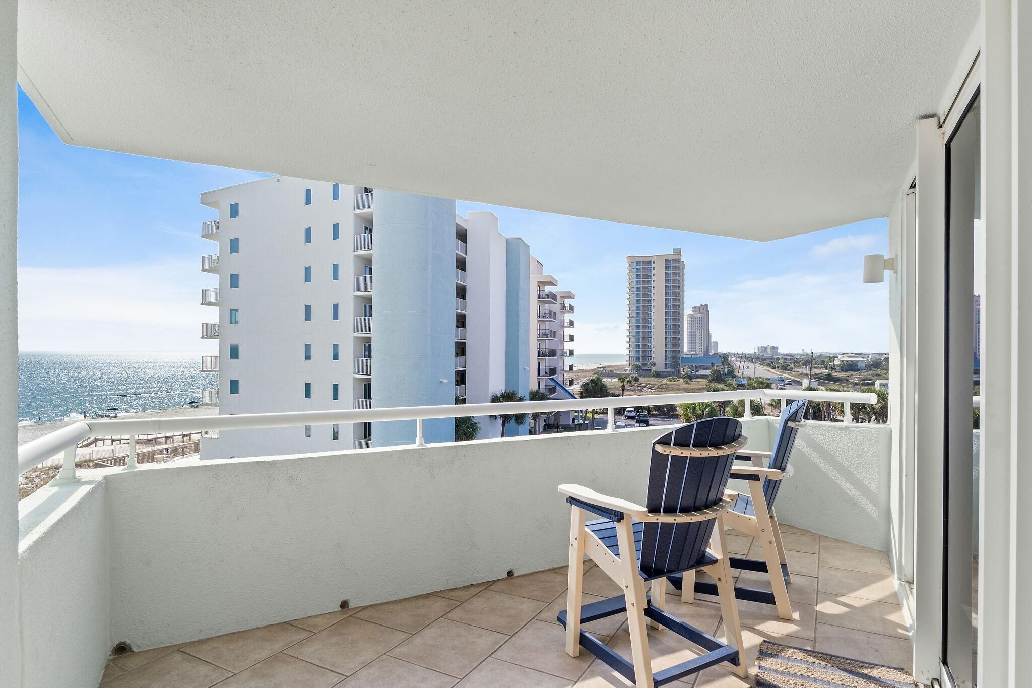 Un balcon avec deux chaises et une vue sur la mer et les bâtiments.