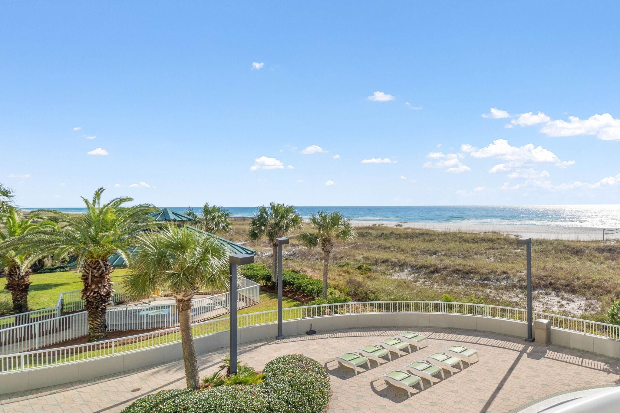 A beach view from a balcony with sun loungers and palm trees.