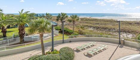 A beach view from a balcony with sun loungers and palm trees.