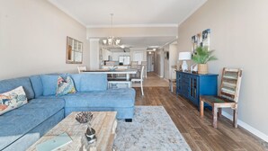 Un salón amplio con un sofá azul, una mesita de centro y una zona de comedor al fondo.