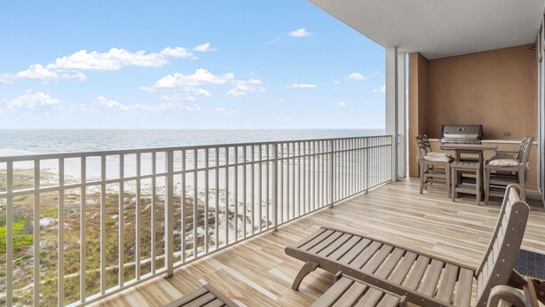 A balcony with a view of the ocean, wooden furniture, and a laptop on a table. - Vista Del Mar 402 (Pensacola)