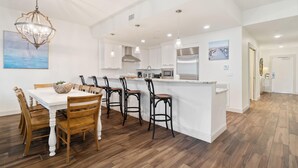 A modern kitchen with white cabinetry, a central island, and bar stools. - Vista Del Mar 402 (Pensacola)