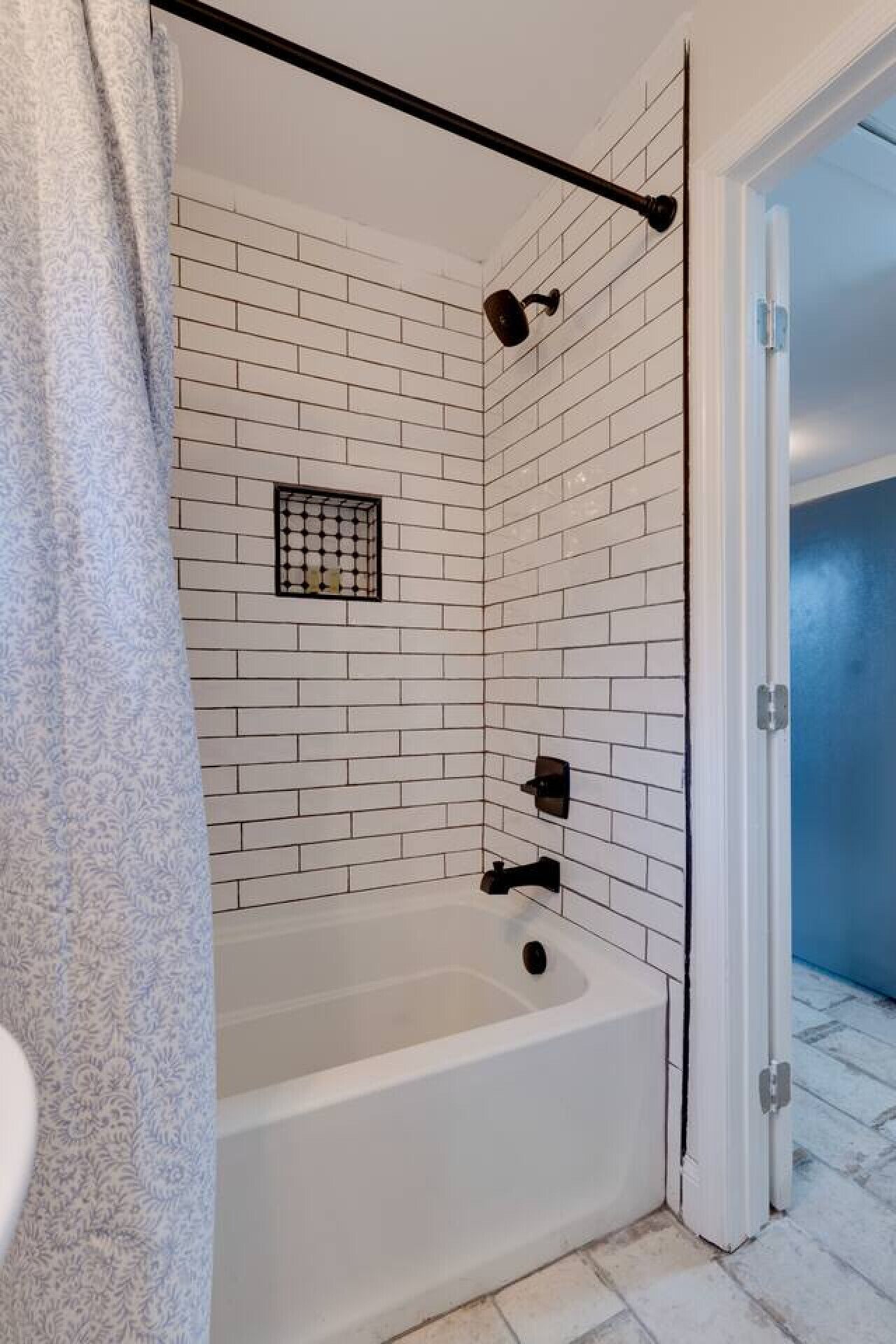 A bathroom with white subway tiles, a bathtub, a showerhead, and a towel rack.