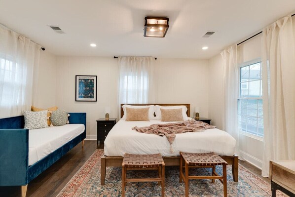 A bedroom with a large bed, a smaller sofa, a nightstand, and a window with curtains.