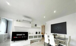 A modern living room with a flat-screen TV, white furniture, and a large abstract painting on the wall.
