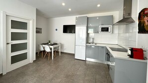 A modern kitchen with a dining area, white cabinetry, a microwave, and a red appliance on the counter.