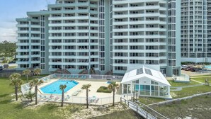 A multi-story hotel with a pool area, including a small building with a glass facade. - Perdido Sun 702 (Pensacola)
