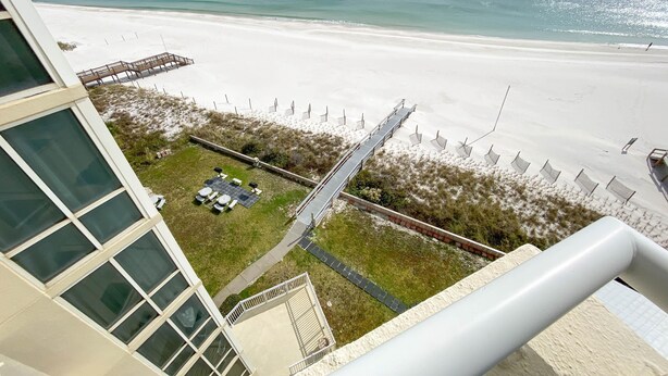 A beach view from a hotel balcony with a deck, a grassy area, and a sandy beach. - Perdido Sun 702 (Pensacola)