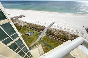 A beach view from a hotel balcony with a deck, a grassy area, and a sandy beach. - Perdido Sun 702 (Pensacola)