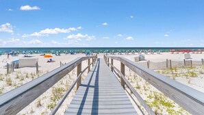 A wooden boardwalk leading to a beach with umbrellas and beach chairs. - Perdido Sun 702 (Pensacola)