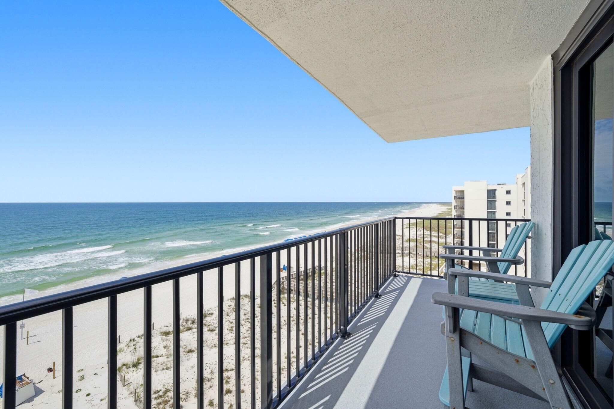 A balcony with a view of the ocean, a railing, and two chairs.