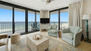 A spacious balcony with a television, two light-colored armchairs, a coffee table, and a lamp. - Lei Lani 607t (Orange Beach)