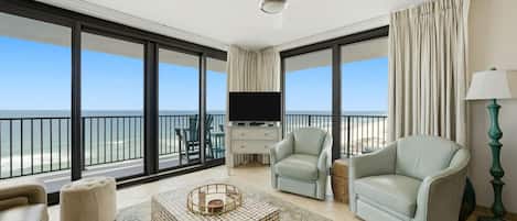 A spacious balcony with a television, two light-colored armchairs, a coffee table, and a lamp.