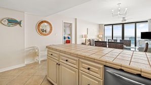 A spacious kitchen with a large island, a dining area with a view, and a living room with a TV. - Lei Lani 607t (Orange Beach)