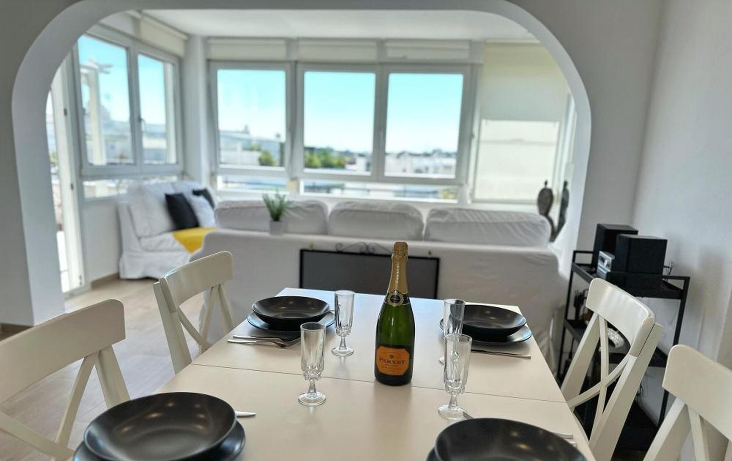 Comedor con una mesa dispuesta para cuatro, una botella de champán y vistas de la ciudad a través de amplios ventanales.