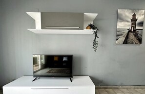 Relax in this serene living space with a flat-screen TV, console table, and a beautiful potted plant.