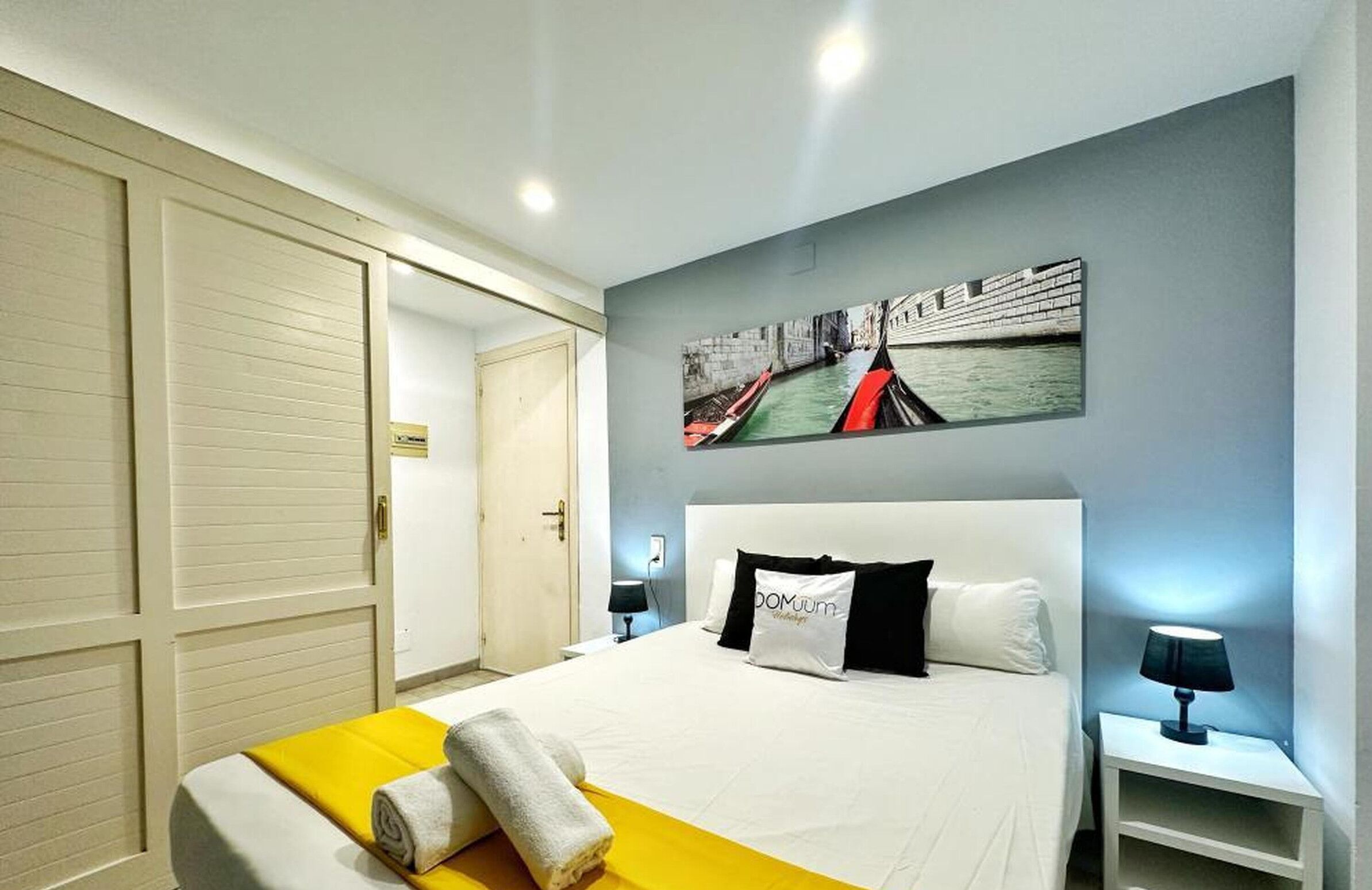 A hotel room with a bed, a nightstand, a wall-mounted painting, and a door.