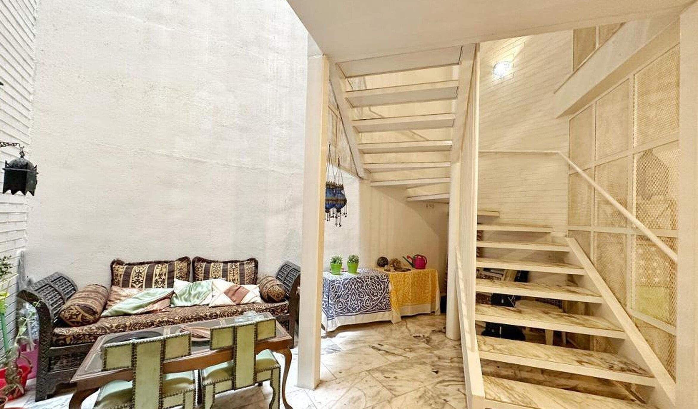 A room with a sofa, chairs, a small table, and a staircase with a wooden railing.