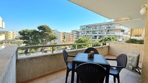 A balcony with a table and chairs, overlooking a residential area with multiple buildings and trees. - Cozy Apartment with Pool, 300m from Levante Beach, Free WiFi, Near Port Aventura (Salou)