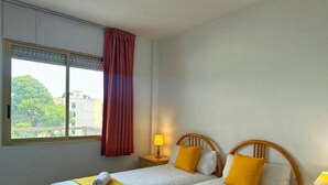 A hotel room with two beds, a window with curtains, and a view of buildings outside. - Cozy Apartment with Pool, 300m from Levante Beach, Free WiFi, Near Port Aventura (Salou)