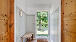 A hallway with wooden walls and doors, a bench, and a view of a garden through an open door.